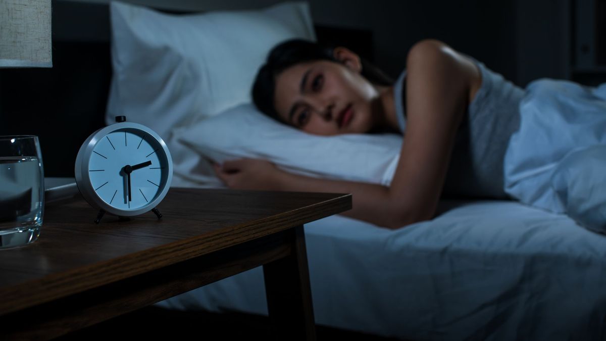 Person liegt nachts wach im Bett und schaut auf die Uhr gegen 3 Uhr – typisches nächtliches Aufwachen und Gedankenkarussell.